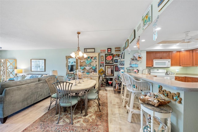 dining area with ceiling fan with notable chandelier, a raised ceiling, and light wood-type flooring