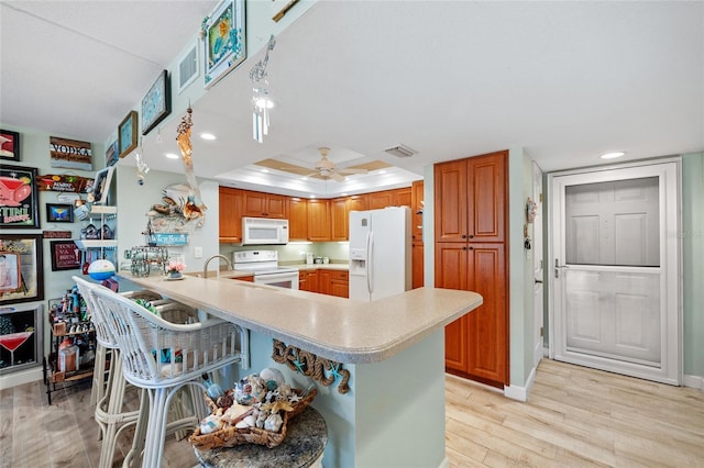 kitchen with light wood-type flooring, visible vents, white appliances, a peninsula, and light countertops