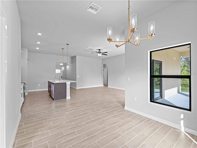 interior space with ceiling fan with notable chandelier, visible vents, open floor plan, light countertops, and hanging light fixtures