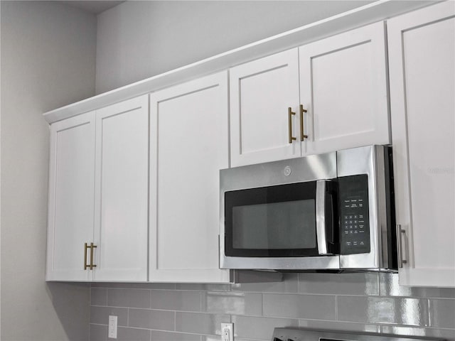 details featuring stainless steel microwave, backsplash, and white cabinets