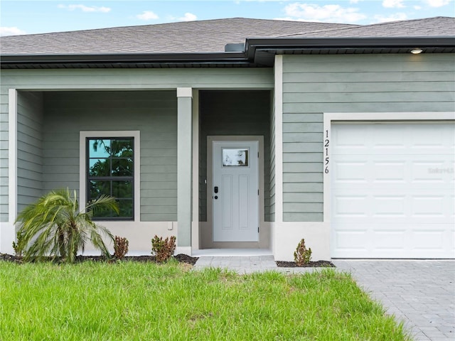 12156 Wellington Ave, Port Charlotte, FL 33981 - doorway to property with an attached garage, roof with shingles, a lawn, and driveway