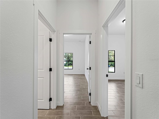 hall featuring a textured wall, wood finish floors, plenty of natural light, and baseboards