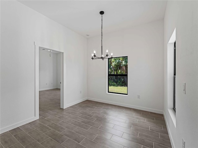 spare room with a chandelier, dark wood-style floors, and baseboards