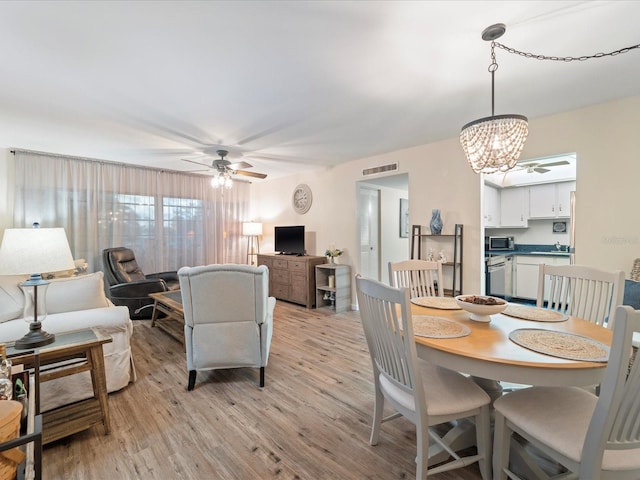 dining room featuring light wood finished floors, visible vents, and ceiling fan with notable chandelier