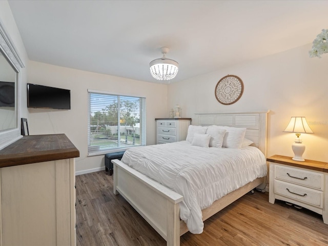 bedroom with baseboards, a notable chandelier, and wood finished floors