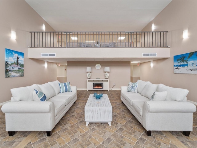 living area with visible vents, baseboards, a towering ceiling, and stone finish flooring