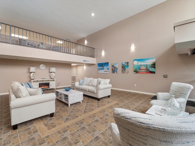 living area with visible vents, baseboards, a high ceiling, and a warm lit fireplace