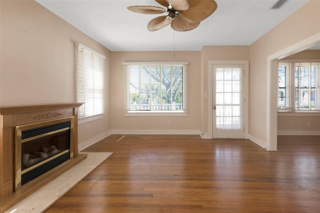 unfurnished living room with a glass covered fireplace, visible vents, baseboards, and wood finished floors