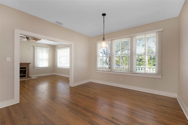 unfurnished dining area with a glass covered fireplace, dark wood finished floors, baseboards, and ceiling fan