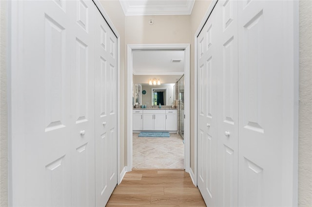 hallway featuring visible vents, light wood-style flooring, and crown molding