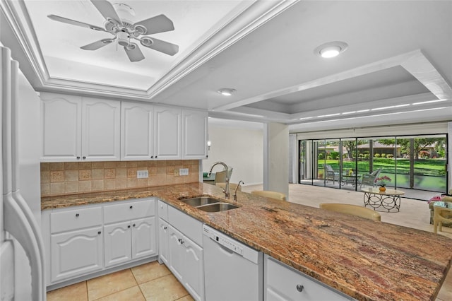 kitchen with white appliances, stone countertops, a tray ceiling, and a sink