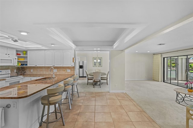 kitchen with white appliances, a sink, white cabinetry, dark stone counters, and a raised ceiling