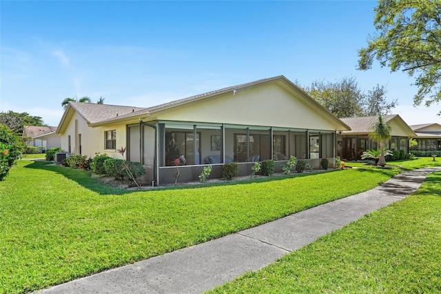 view of front of house featuring a sunroom, a front yard, central AC unit, and stucco siding