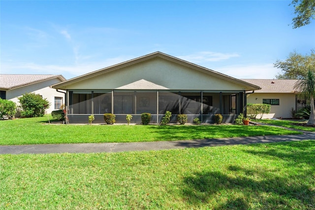 rear view of house featuring a lawn, a sunroom, and stucco siding