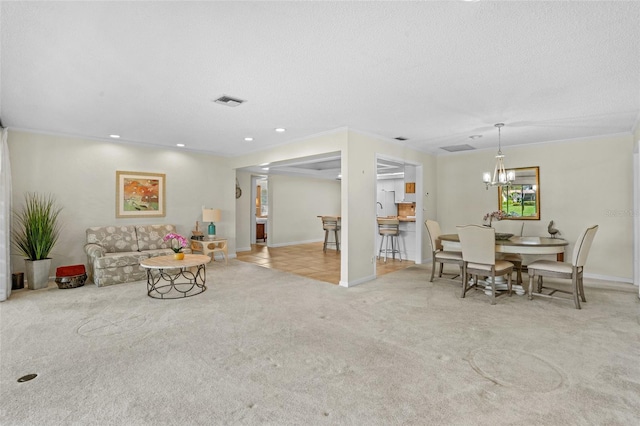 living area with visible vents, an inviting chandelier, carpet flooring, a textured ceiling, and baseboards