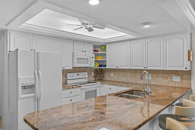 kitchen with a peninsula, white appliances, stone countertops, and a sink