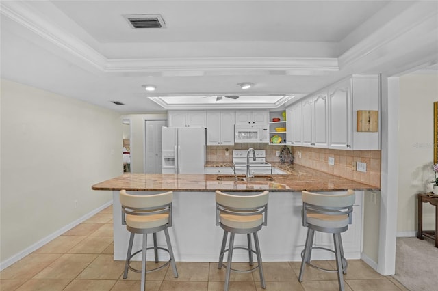 kitchen with a raised ceiling, visible vents, dark stone counters, white appliances, and a peninsula