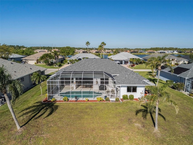 rear view of property with a residential view, glass enclosure, an outdoor pool, and a lawn