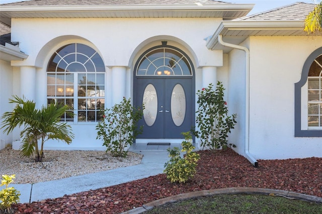 view of exterior entry with stucco siding and roof with shingles