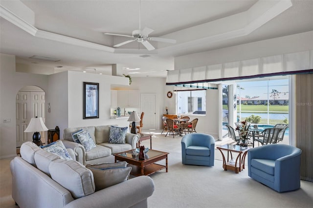 living room with a raised ceiling, light colored carpet, a water view, and ceiling fan