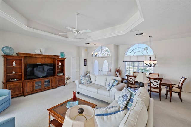 carpeted living area with a tray ceiling, visible vents, and ceiling fan with notable chandelier