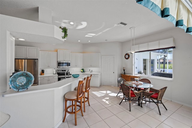 kitchen with visible vents, light countertops, light tile patterned floors, a kitchen breakfast bar, and stainless steel appliances