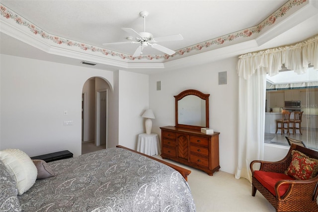 carpeted bedroom featuring a tray ceiling, arched walkways, visible vents, and a ceiling fan