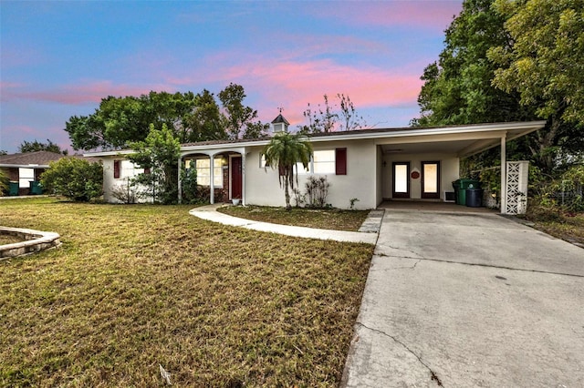 ranch-style house featuring stucco siding, an attached carport, a lawn, and concrete driveway