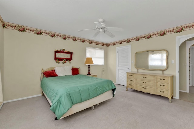 bedroom with a closet, baseboards, light colored carpet, and ceiling fan