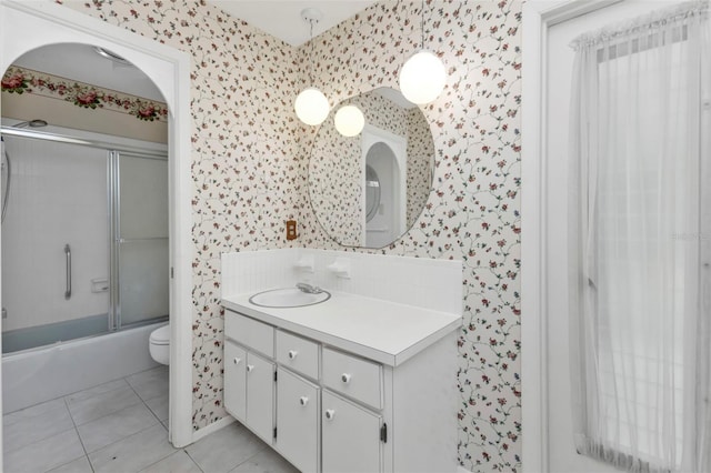 bathroom featuring tile patterned floors, toilet, combined bath / shower with glass door, wallpapered walls, and vanity