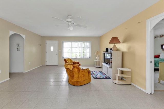 sitting room with baseboards, arched walkways, ceiling fan, and light tile patterned flooring