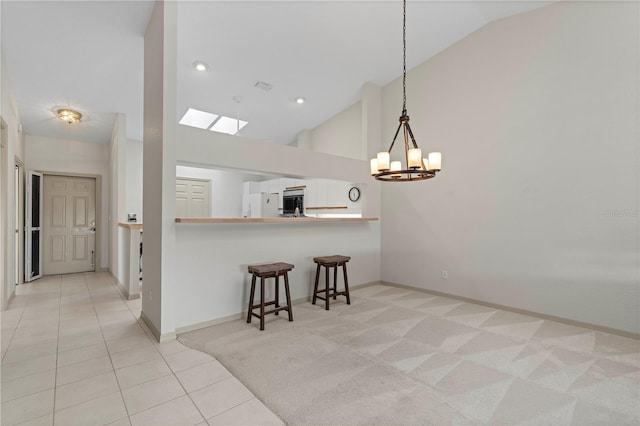 kitchen featuring a notable chandelier, light tile patterned floors, light carpet, high vaulted ceiling, and a kitchen breakfast bar