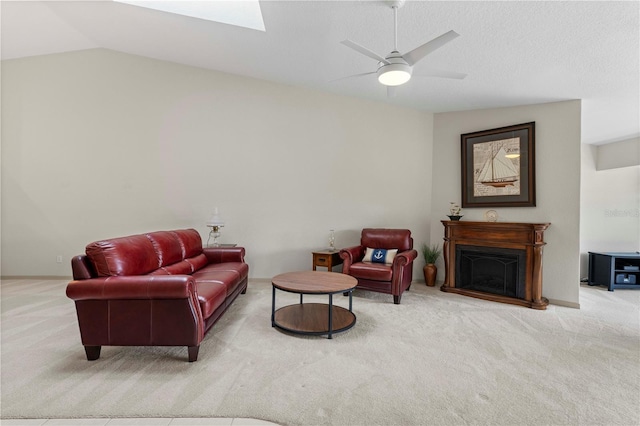 living room featuring lofted ceiling with skylight, carpet, a fireplace, and a ceiling fan