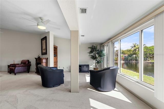 carpeted living room with a wealth of natural light, a water view, visible vents, and a ceiling fan