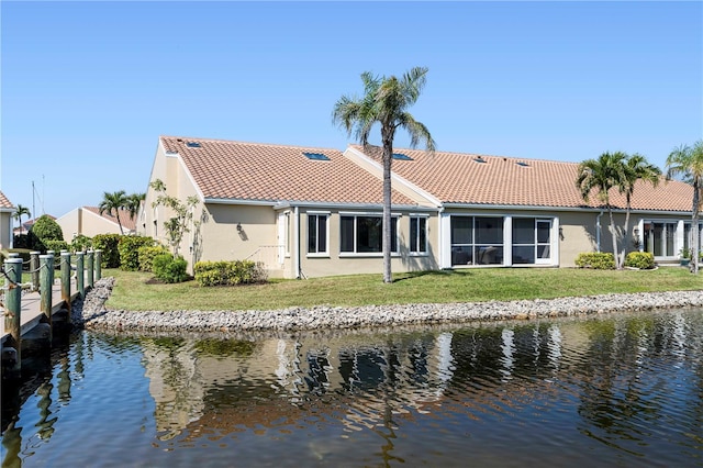 rear view of house with a yard, a water view, a tile roof, and stucco siding