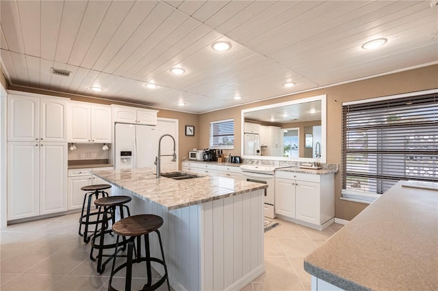 kitchen featuring white appliances, a breakfast bar area, visible vents, light tile patterned flooring, and a sink