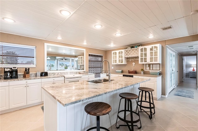 kitchen with glass insert cabinets, an island with sink, a kitchen bar, white cabinetry, and a sink