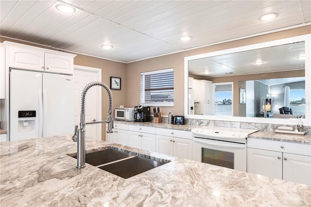 kitchen with a sink, white appliances, white cabinetry, and light stone countertops