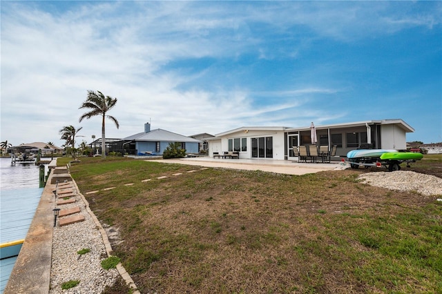 exterior space featuring a sunroom, a patio area, a lawn, and a water view