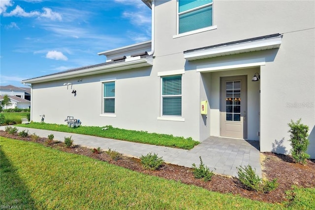 doorway to property featuring stucco siding and a lawn