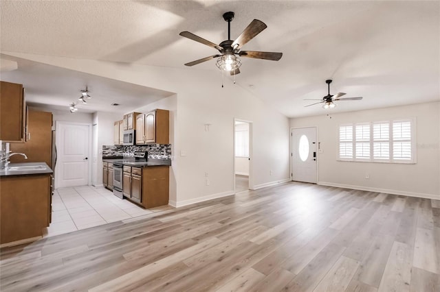 kitchen with dark countertops, open floor plan, brown cabinets, appliances with stainless steel finishes, and a sink