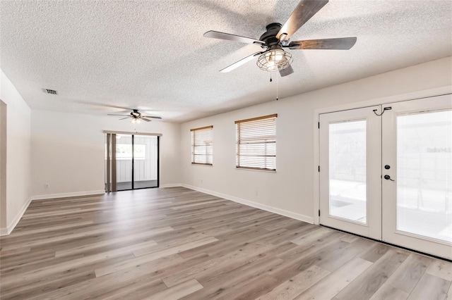 spare room with visible vents, light wood-style flooring, a textured ceiling, french doors, and baseboards