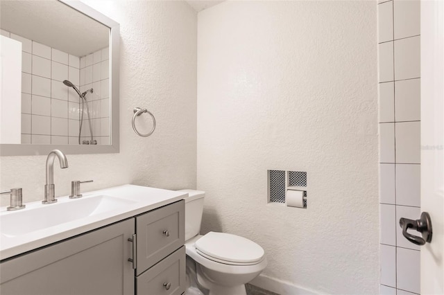 bathroom with a tile shower, toilet, vanity, and a textured wall