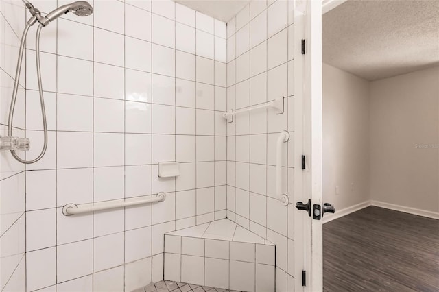 bathroom with baseboards, a textured ceiling, wood finished floors, and a tile shower