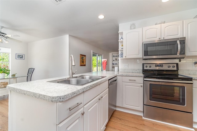 kitchen with light wood-type flooring, a sink, open shelves, stainless steel appliances, and a peninsula