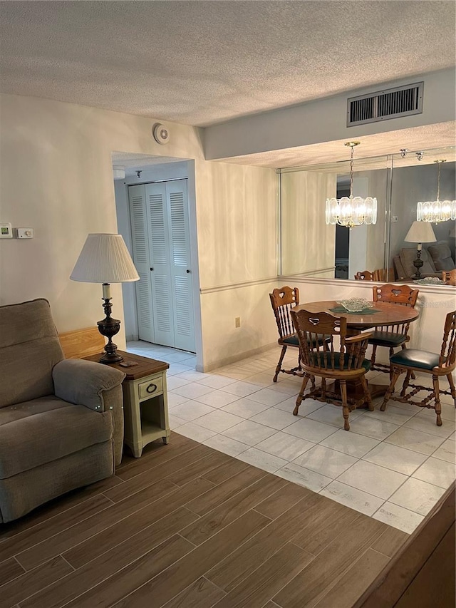 dining area with light wood-style flooring, a notable chandelier, visible vents, and a textured ceiling