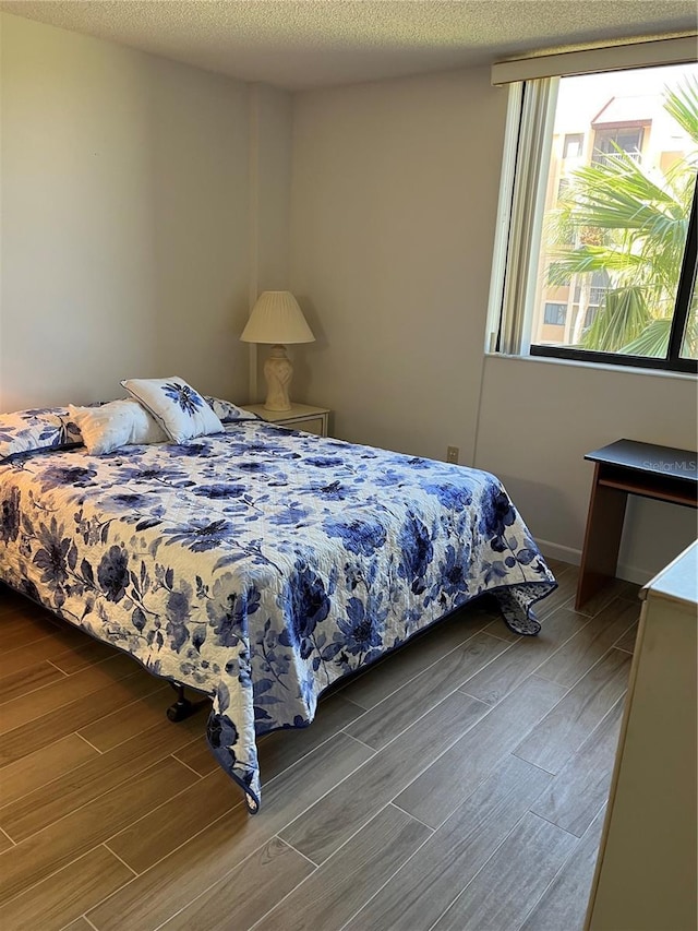 bedroom with baseboards, a textured ceiling, and wood finish floors