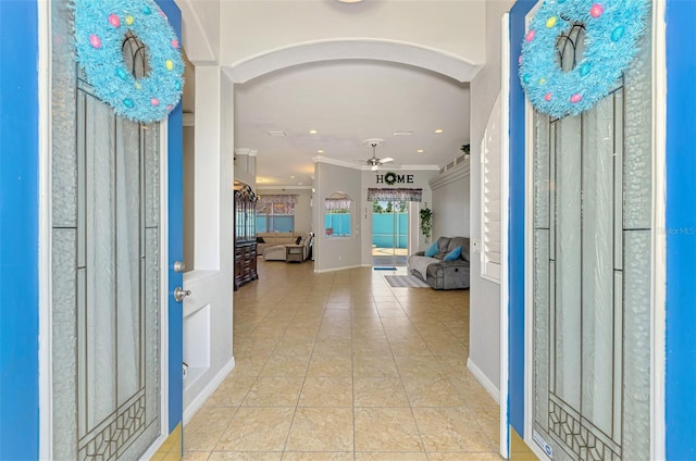 entryway featuring tile patterned floors, baseboards, ceiling fan, ornamental molding, and arched walkways