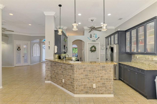 kitchen with ornamental molding, a ceiling fan, light stone counters, arched walkways, and decorative backsplash