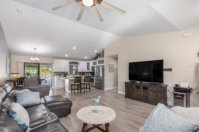 living area featuring baseboards, ceiling fan with notable chandelier, light wood-style floors, and vaulted ceiling